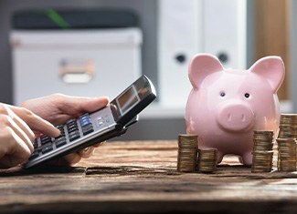 Person using a calculator with a piggy bank and coin stacks nearby
