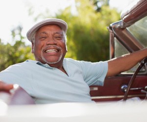 Senior man with hat smiling while driving car