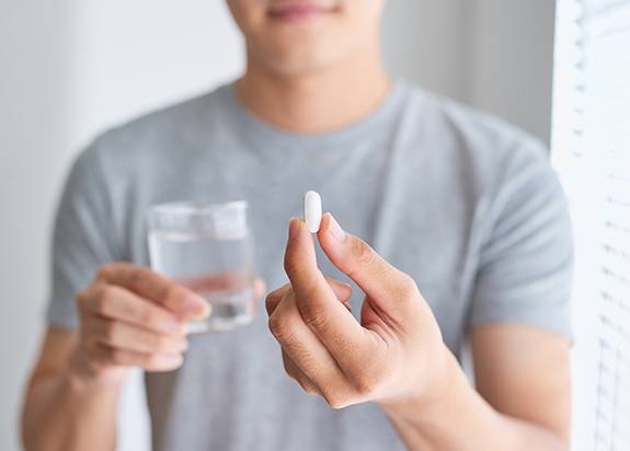 a man holding a glass of water in one hand and a pill in the other