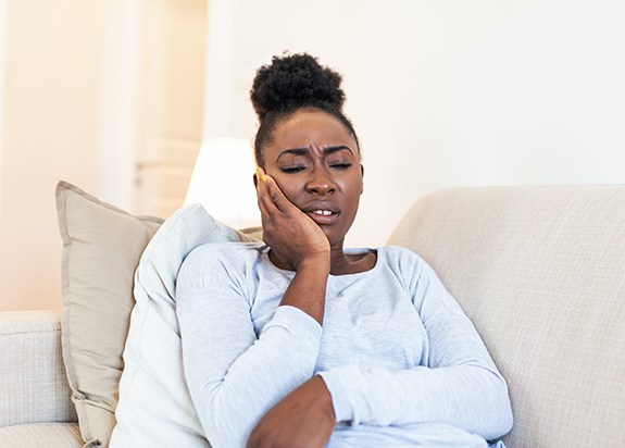 Woman experiencing toothache on couch at home